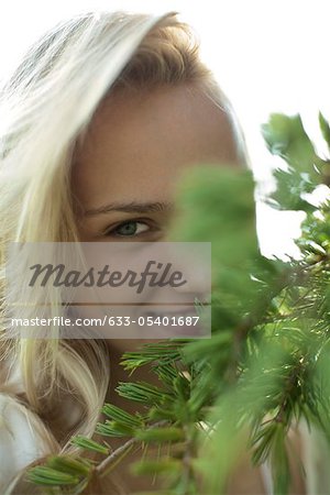 Smiling young woman behind tree branches, cropped