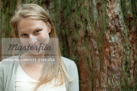 Young woman leaning against tree trunk, portrait