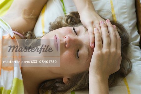 Young woman lying in bed with hands clasped on forehead