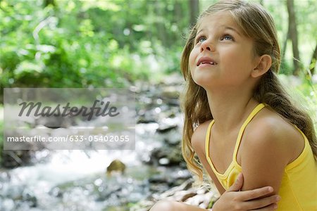 Girl beside stream, looking up in awe