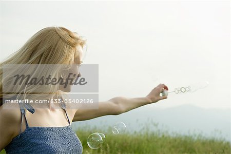 Young woman holding out bubble wand in wind