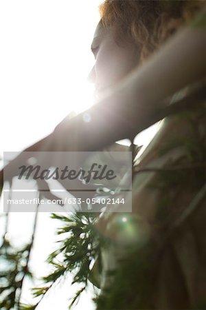 Woman touching tree branch, silhouetted by sun