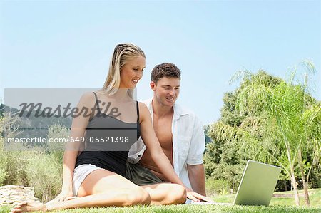 Couple using laptop in grass together