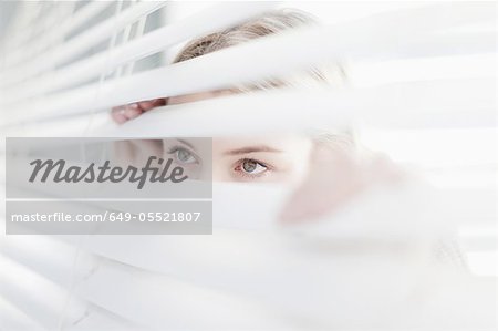 Teenage girl peering through blinds