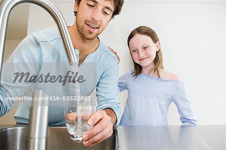 Young man filling glass of water for daughter Young man filling glass of water for daughter