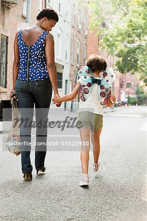 Mother and daughter walking along street, rear view