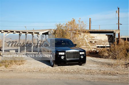 Rolls Royce parked on roadside in front of abandoned house