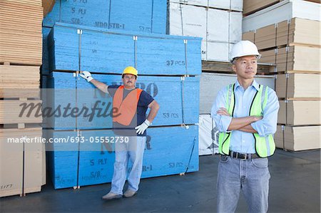 Male warehouse workers standing in front of stack of plywood