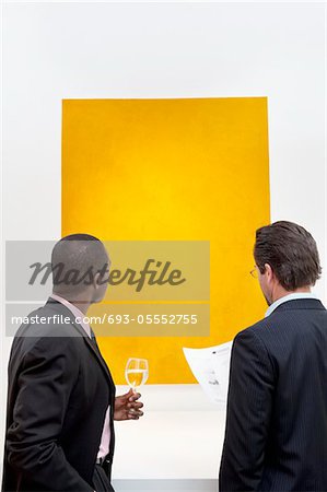 Two people looking at yellow painting on wall in art gallery