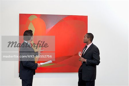Two males talking over painting in art gallery