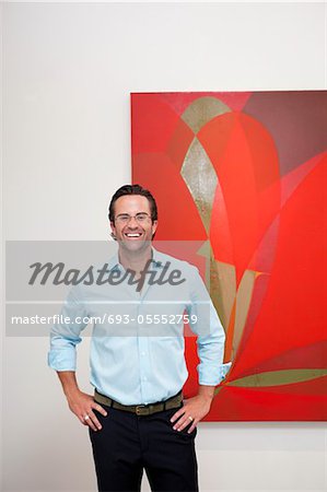 Smiling man with hands on hips in front of wall painting