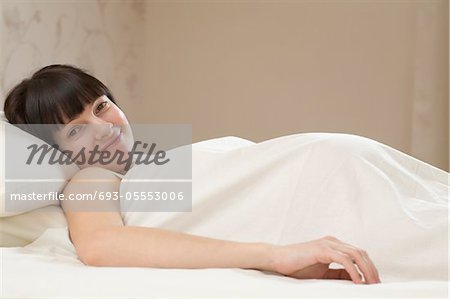 Porträt der lächelnde junge schwangere Frau auf dem Bett liegend