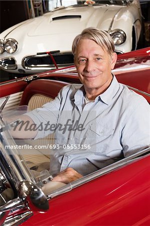 Portrait of smiling elderly man sitting in car in shop