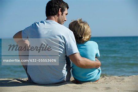 Père et fils s'asseoir ensemble à la plage, vue arrière