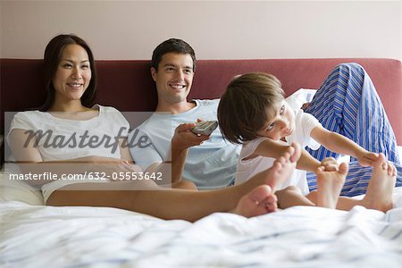Family watching TV together in bed