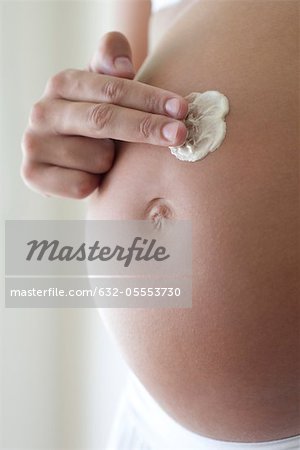 Woman applying moisturizer to pregnant belly, cropped