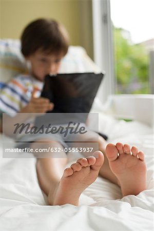 Boy relaxing on bed with digital tablet