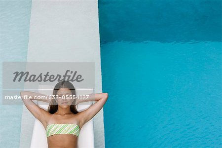 Jeune femme allongée avec satisfaction sur une chaise longue près de la piscine