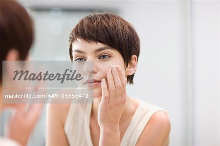 Woman applying moisturizer in mirror