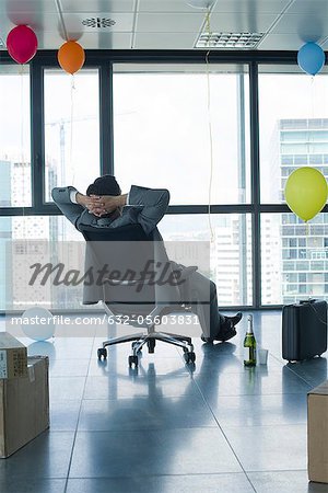 Businessman sitting in new office with balloons and boxes