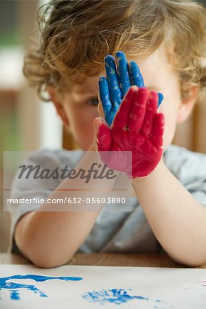 Little boy holding paint covered hands in front of his face