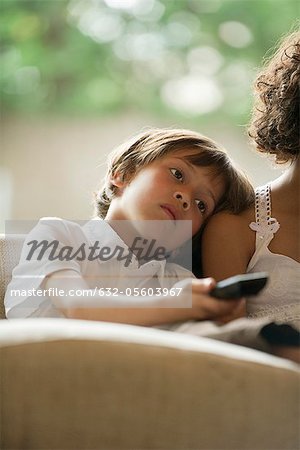 Boy watching TV, resting head on his sister's shoulder