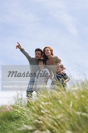 Parents and two boys standing on meadow, father pointing into distance