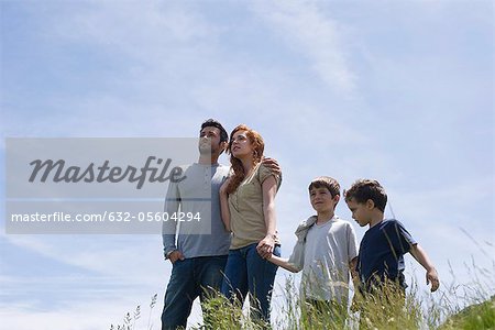 Parents and two boys standing on meadow holding hands, low angle view