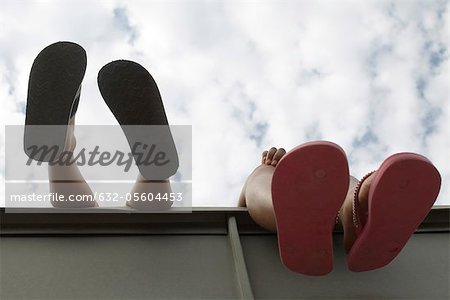 Children's feet dangling over ledge, low angle view