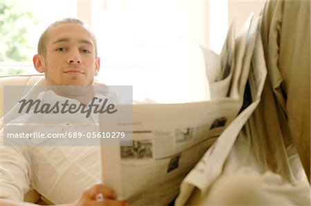 Young man reading newspaper on couch