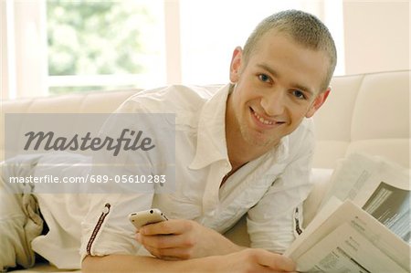 Man with cell phone and newspaper on couch