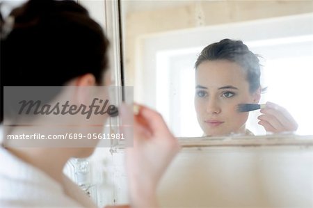 Young woman applying blush in bathroom