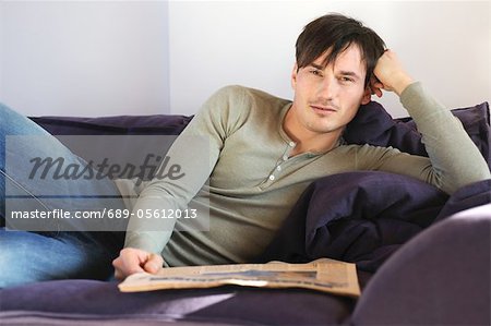 Young man on couch reading newspaper