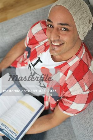 Smiling man holding book sitting on couch