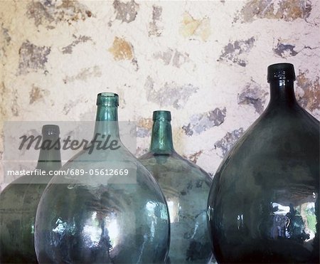 Vier Runde Glasflaschen vor Steinmauer