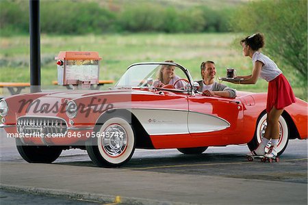 1990s COUPLE IN 1950s CORVETTE WAITRESS ON ROLLER SKATES AT CAR HOP GRANBY COLORADO USA