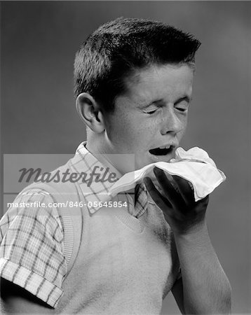 1950s BOY WEARING SWEATER VEST WITH A COLD SNEEZING INTO A HANDKERCHIEF INDOOR