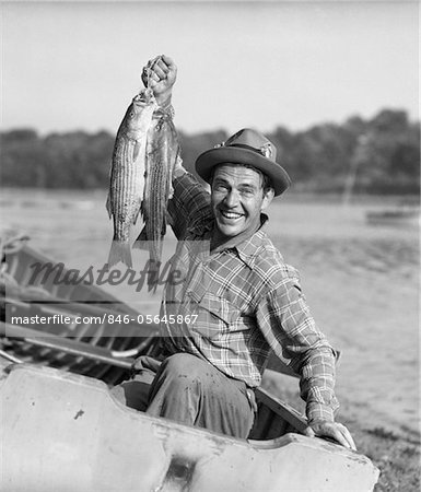 1940s - 1950s HAPPY MAN FISHING FROM A ROWBOAT SMILING HOLDING UP FISH JUST CAUGHT WITH PRIDE