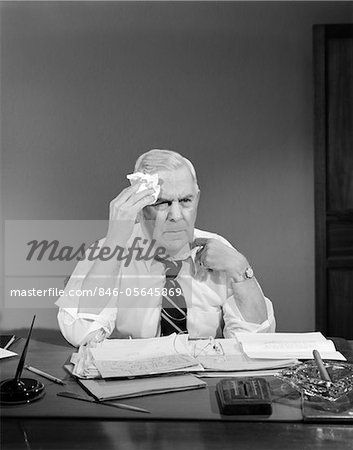 1950s BUSINESSMAN SITTING AT DESK WIPING FOREHEAD WITH HANDKERCHIEF PULLING AT SHIRT COLLAR