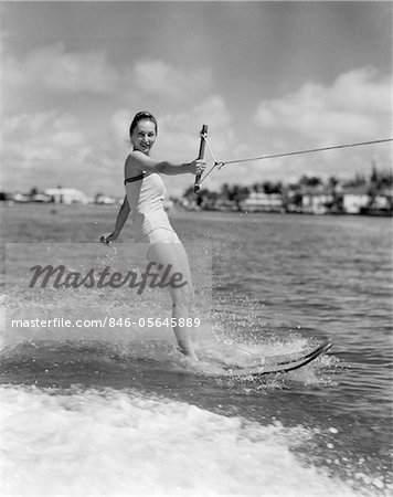 ANNÉES 1950 SOURIANT FEMME EN MAILLOT DE BAIN SKI NAUTIQUE EN AGITANT UNE MAIN