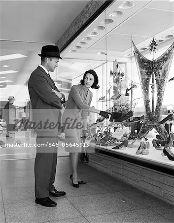 1950s COUPLE MAN WOMAN WINDOW SHOPPING WOMAN POINTING TO PAIR OF SHOES IN STORE WINDOW DISPLAY