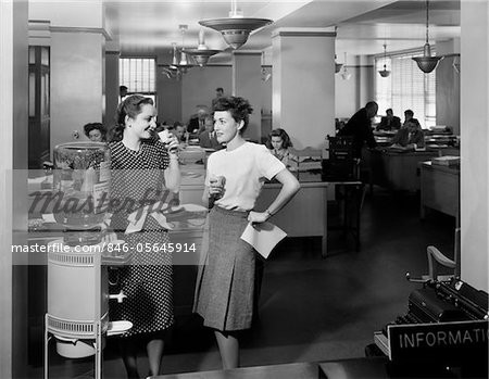 1940s TWO WOMEN OFFICE WORKERS STANDING BY OFFICE WATER COOLER TALKING