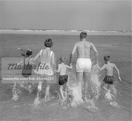 1960s BACK VIEW OF FAMILY OF 5 HOLDING HANDS RUNNING INTO OCEAN