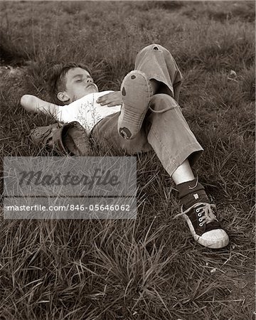 1960s BOY SLEEPING IN GRASS LEGS CROSSED HOLES IN SNEAKERS BASEBALL MITT BY HIS SIDE