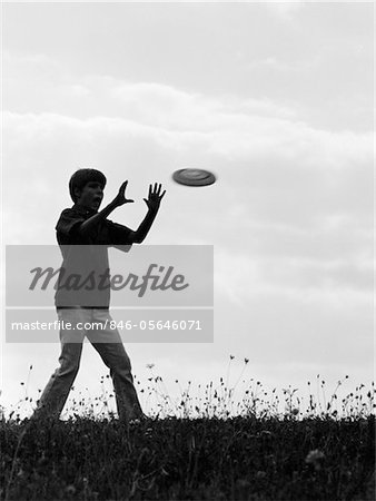 60ER JAHRE - 70ER JAHRE SILHOUETTE DER JUNGE FANG FRISBEE IN FELD