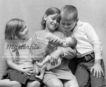 1970ER JAHRE MÄDCHEN BABYFLASCHE ZU BABY-SCHWESTER MIT BRUDER & SCHWESTER SITTING ON BEIDERSEITS IHRE SUCHE WEITER