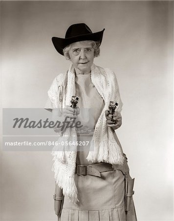 1950s GRANNY COWGIRL WEARING HAT & SHAWL & POINTING 2 PISTOLS AND LOOKING AT CAMERA