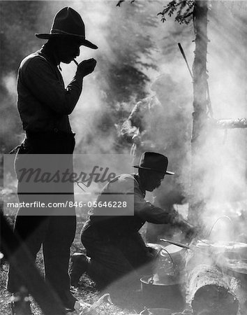 ANNÉES 1920 TROIS HOMMES COWBOYS CAMPING UN HOMME FUMANT PIPE UN HOMME CUISSON SUR FEU DE CAMP MOODY SILHOUETTE