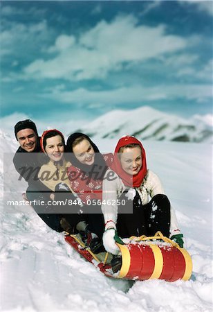 1940s GROUP OF THREE WOMEN ONE MAN ON RED AND YELLOW TOBOGGAN SLEDDING IN THE WINTER SNOW