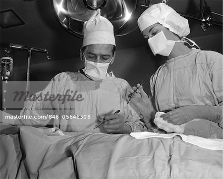 1950ER JAHRE ARZT UND KRANKENSCHWESTER STANDING OVER PATIENT ZU BETREIBEN